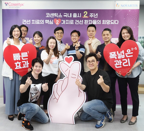 한국노바티스 임직원들이 코센틱스가 제공하는 건선 치료 혜택의 핵심 두 가지를 의미하는 두 손가락으로 손하트를 만들며 급여 2주년을 기념하고 있다.